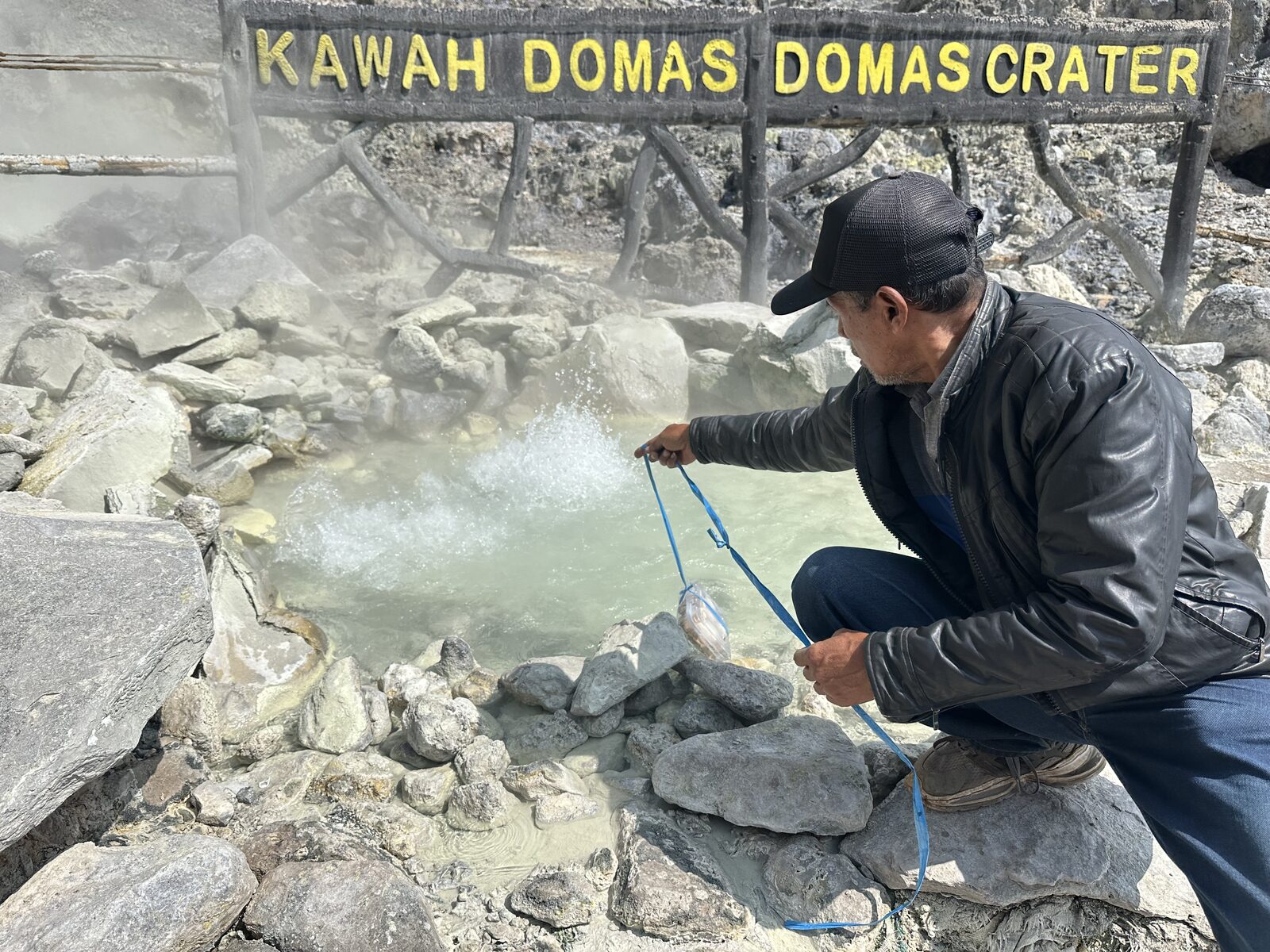 Our Indonesian tour guide attempting to boil our eggs in the volcanic pool, by lowering our eggs in a container into the pool with string.