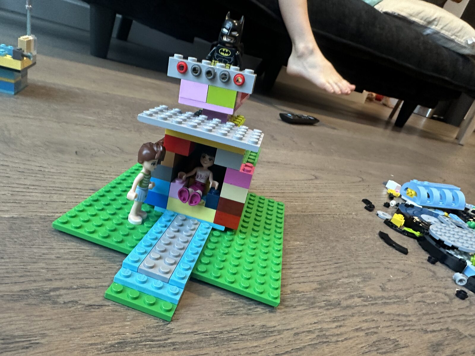 A photo of a pile of Lego on the floor, and a house-type creation with Batman on top next to it, built out of Lego.