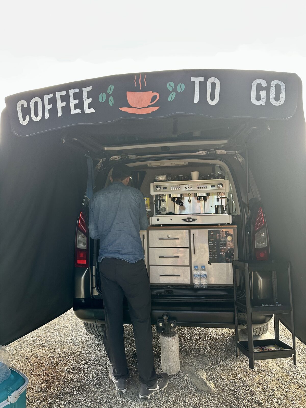 An image of a Moroccan man making coffe from his barista coffee machine in the back of his car