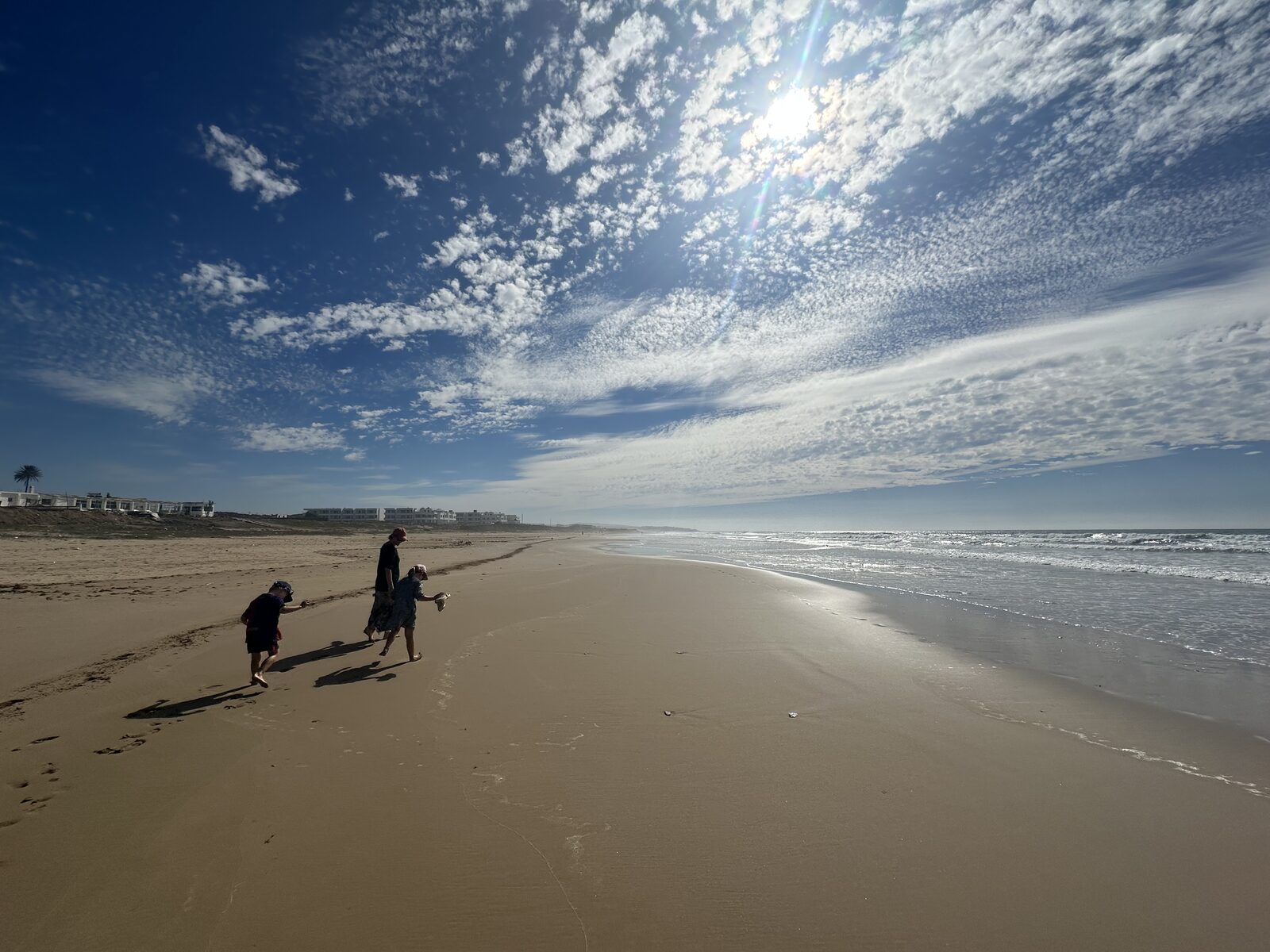 Vikki walking along the beach with her two children, with the Atlantic Ocean on the right and some Moroccan villas in the distance.