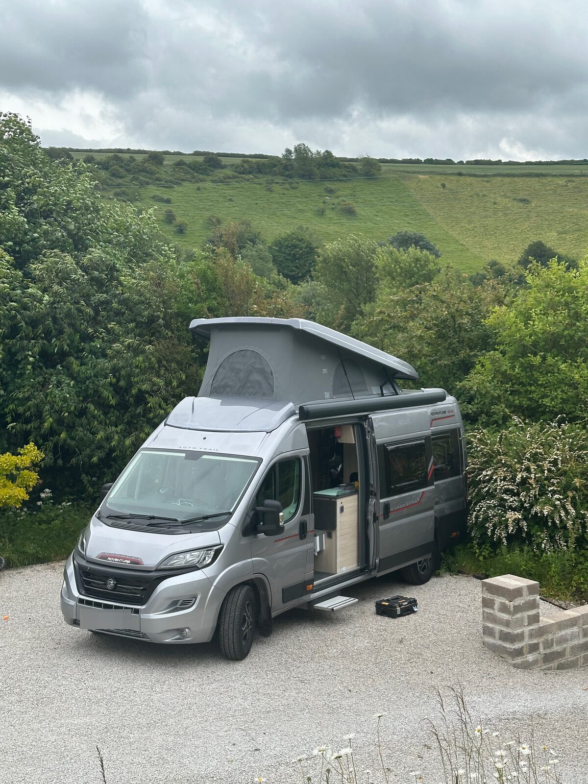 A great Fiat Ducato Adventure 65 camper van sitting on the driveway, with green hills rising behind
