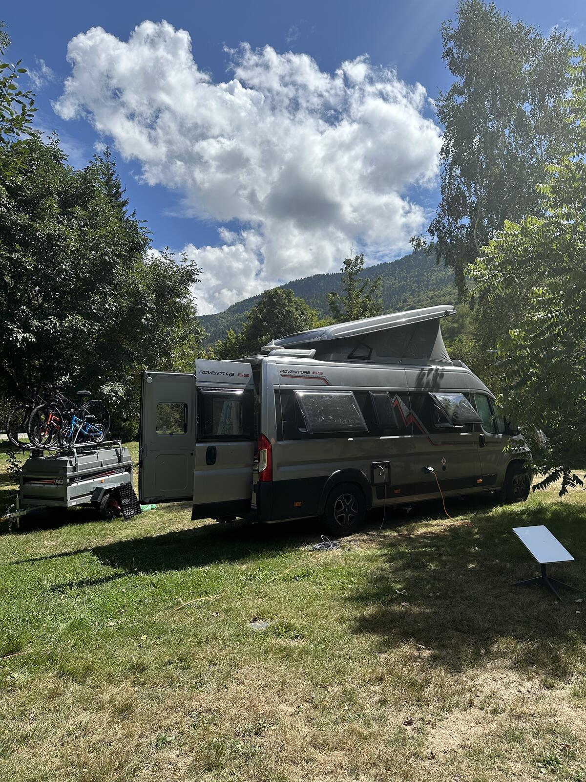 The adventure 65 camper van camped on a grassy field amongst trees, with the Pyrenees rising behind