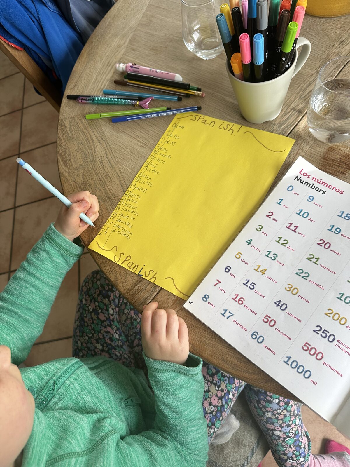 A crib sheet being written on a table, copied from a book, of Spanish numbers