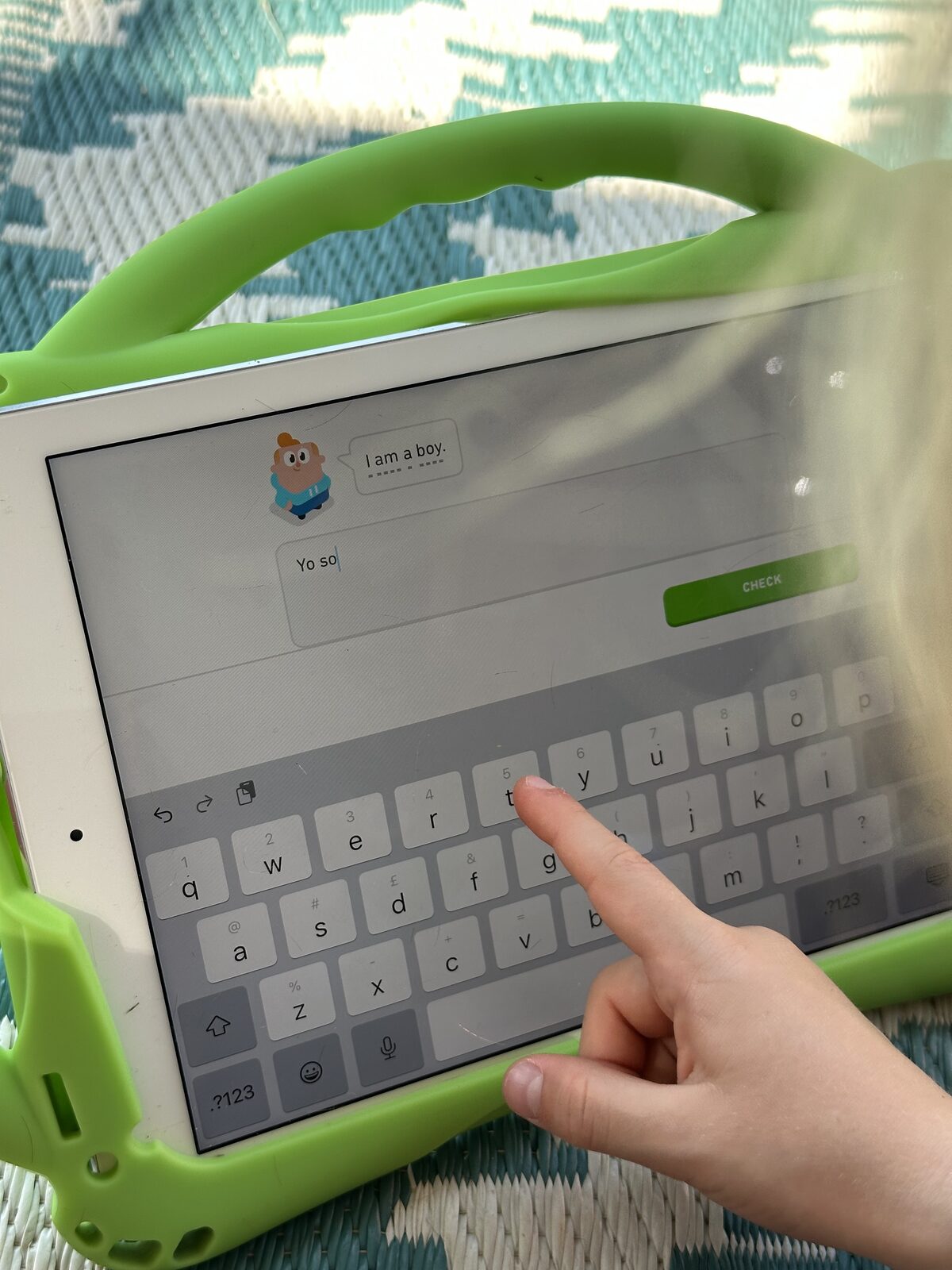An iPad screen with a DuoLingo Spanish app showing, and a child’s finger typing