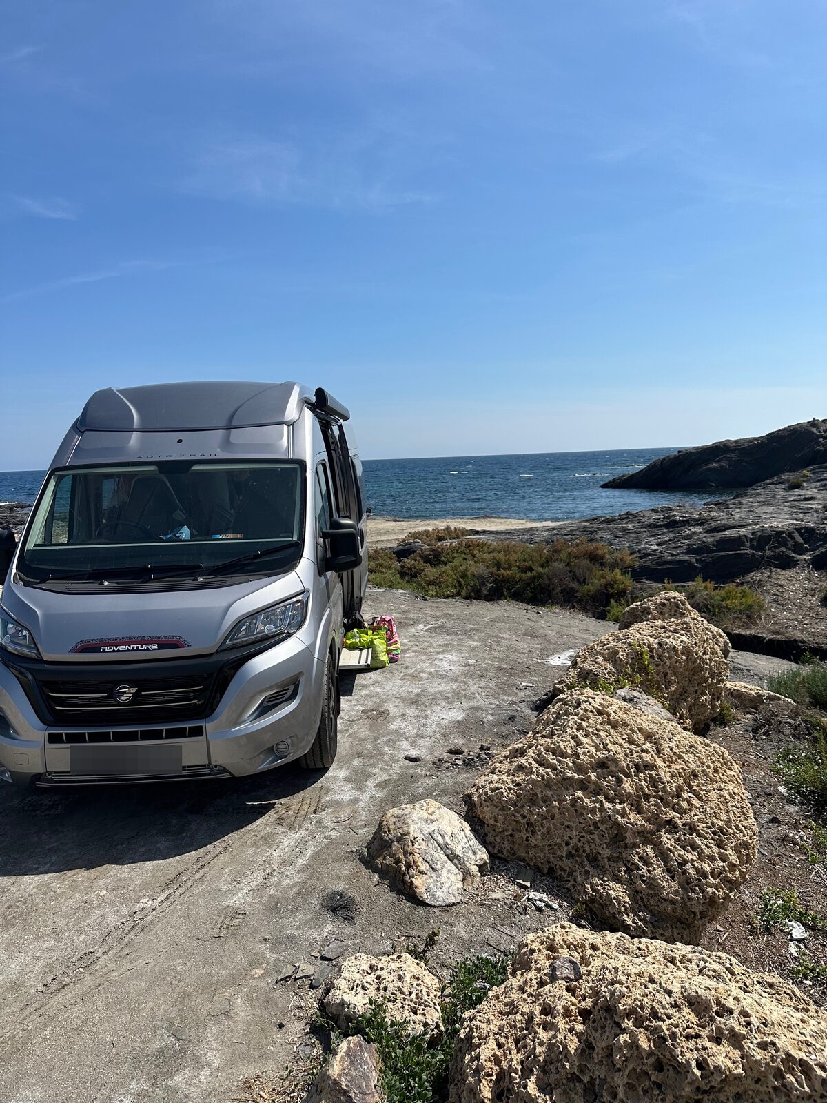 A silver Fiat Ducato adventure 65 van parked on the beach, with bright blue sky and Mediterranean Sea behind